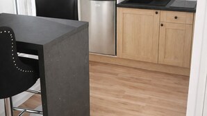 Eine moderne Küche mit Holzausstattung, einem Edelstahlkühlschrank, einer Mikrowelle und einer schwarzen Arbeitsplatte.