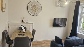 Ein modernes Zimmer mit Esstisch, Stühlen, Fernseher, Sofa und einem Fenster mit Vorhängen.