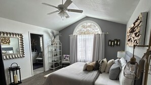 A bedroom with a bed, a ceiling fan, a window with curtains, a mirror, and a wall-mounted light fixture. - Spacious, 9-bed double house in peaceful setting, 12 miles from Frankenmuth (Clio)