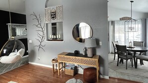 A modern living room with a hanging chair, a dining area with a table and chairs, a wall-mounted mirror, and a decorative wall piece. - Spacious, 9-bed double house in peaceful setting, 12 miles from Frankenmuth (Clio)