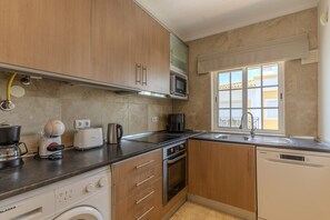 A compact kitchen with a microwave, toaster, coffee maker, and dishwasher. - #318 Spacious 2BR Apartment | Bright Interiors (Albufeira)