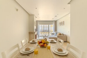 Un coin repas avec une table mise pour le petit-déjeuner, un canapé en arrière-plan et une vue à travers une porte vitrée.