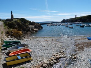 Une plage de rochers, avec des bateaux et un phare en arrière-plan.