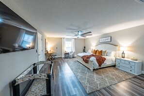 Et soveværelse med seng, sengeborde, ventilator i loftet, et vindue med gardiner og et spejl.