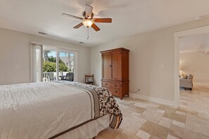 Ein Schlafzimmer mit Bett, Deckenventilator, Holzschrank und einer Schiebetür zum Außenbereich.
