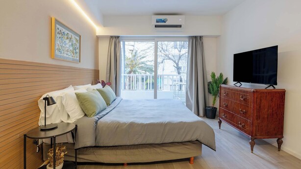 A bedroom with a bed, bedside table, dresser, TV, and a balcony with a view. - MOT Rentals + Plaza Armenia 2B - Loft in Palermo Soho (Buenos Aires)