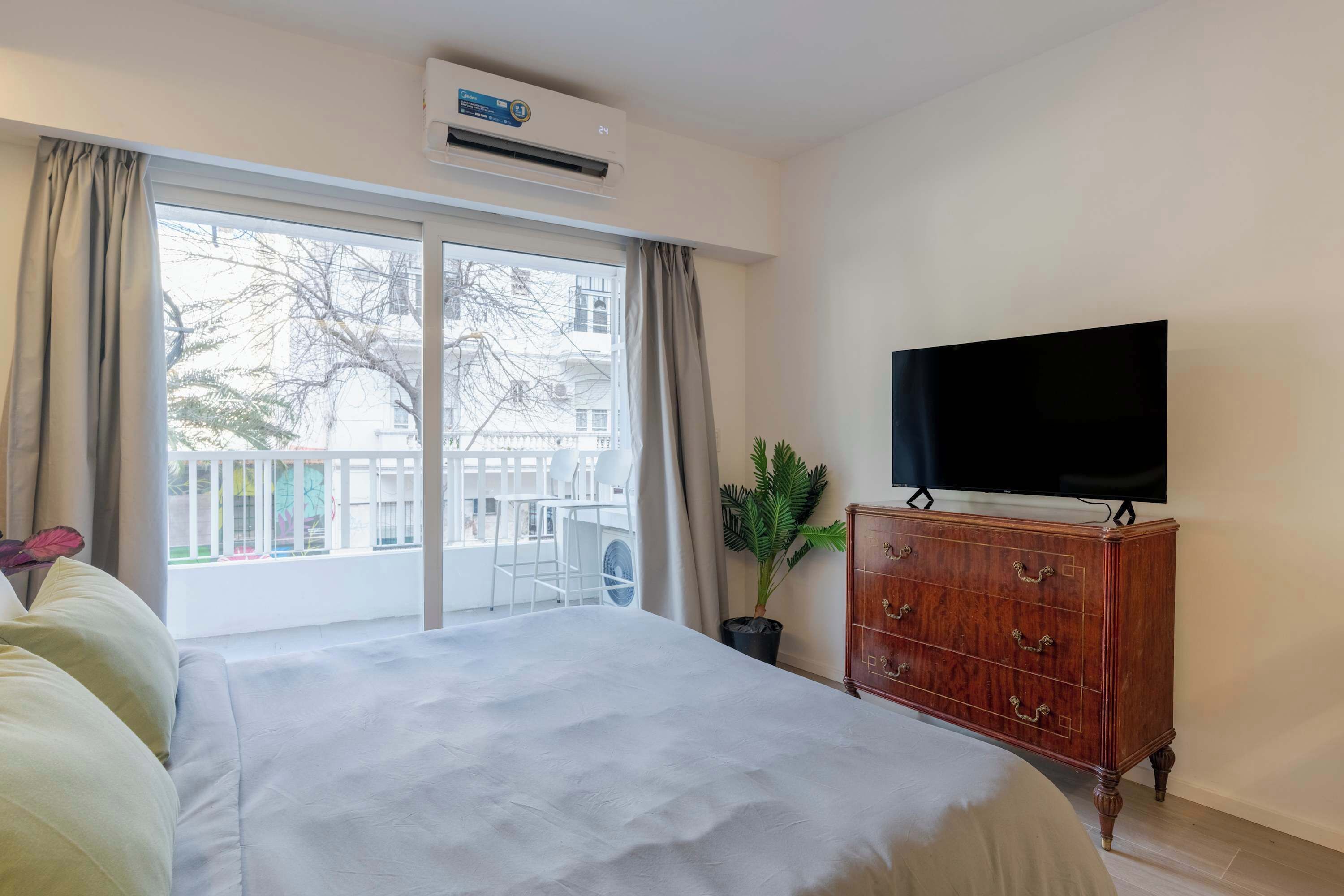 A hotel room with a bed, a TV, a dresser, and a balcony with a view.