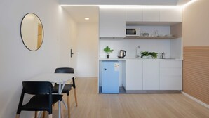 Eine kompakte Küche mit Mikrowelle, Spüle und kleinem Kühlschrank. Ein Esstisch mit Stühlen und ein Spiegel an der Wand sind vorhanden.