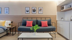 Una sala de estar moderna con sofá, una mesita de centro, una planta y una cocina con armarios y microondas.