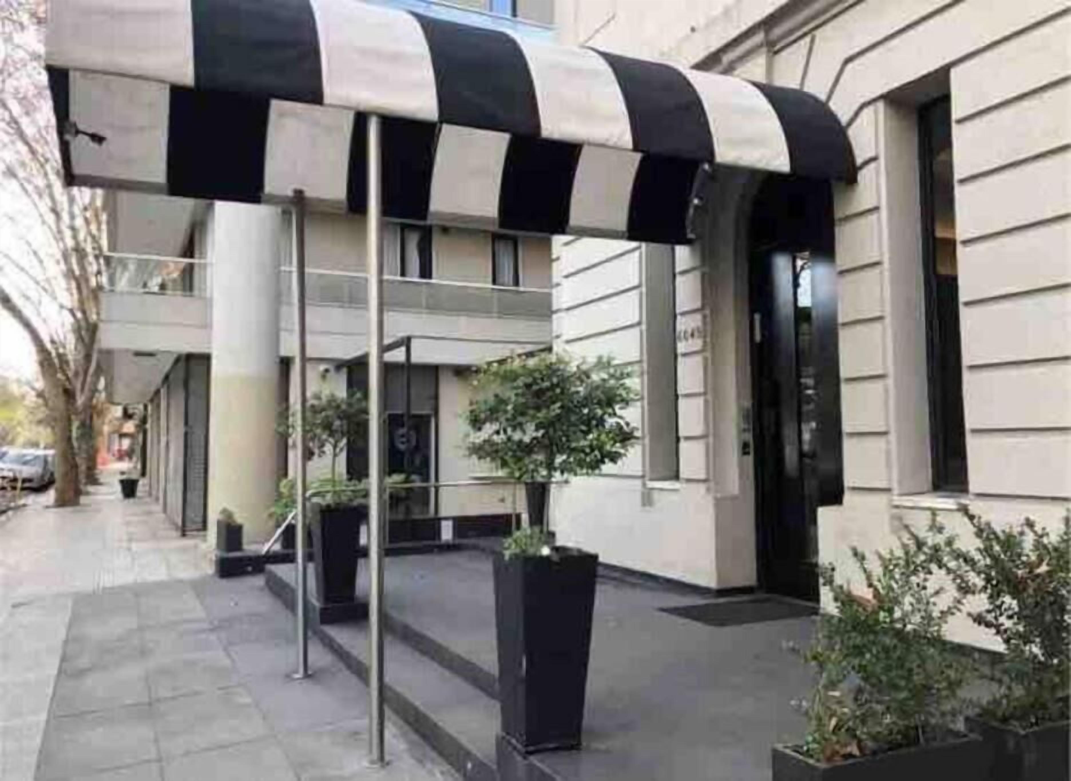 Un edificio con toldo a rayas negras y blancas, plantas en macetas y un estilo arquitectónico moderno y limpio.