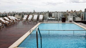 En pool på taket med solstolar och utsikt över staden.