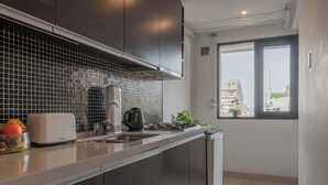Ett modernt kök med mörka skåp, kakel ovanför arbetsbänken, en brödrost, en vattenkokare och ett fönster med utsikt över byggnader.