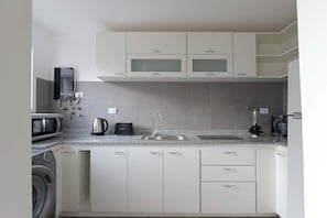Eine moderne Küche mit weißen Schränken, einer eingebauten Mikrowelle, einem Wasserkocher und einer Kaffeemaschine.