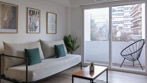 A modern living room with a sofa, a coffee table, and a chair. There are framed artworks on the wall and a large window with a view of buildings. - MOT Rentals + Arevalo 2300 - 3 pax Loft Palermo Hollywood (Buenos Aires)