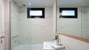 Uma casa de banho moderna com chuveiro em cabine de vidro, lavatório branco e espelho com moldura de madeira.