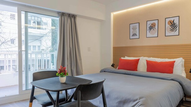 A modern hotel room with a large bed, a small table with a potted plant, and a window with a view of buildings. - MOT Rentals Plaza Armenia 1A - Loft in Palermo Soho (Buenos Aires)