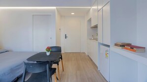 A small, modern room with a bed, a table with chairs, a small kitchen area, and a door. - MOT Rentals Plaza Armenia 1A - Loft in Palermo Soho (Buenos Aires)