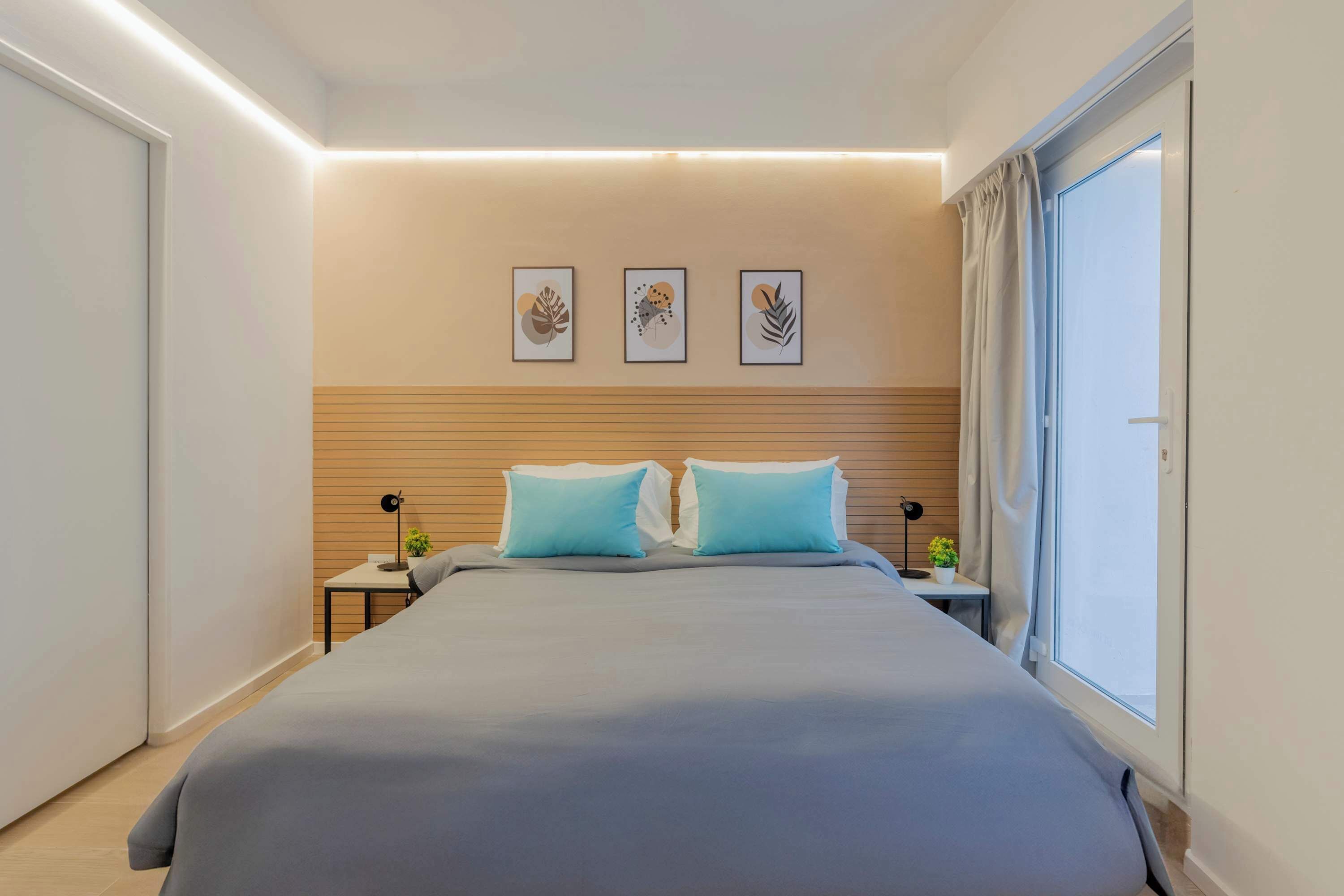 Une chambre moderne avec un grand lit, des tables de chevet, une commode, des œuvres d’art murales et une fenêtre avec des rideaux.