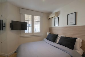 A bedroom with a bed, a TV mounted on the wall, an air conditioner, and two framed pictures. - LDV Aparts 2C Entrepiso by MOT Rentals (Buenos Aires)