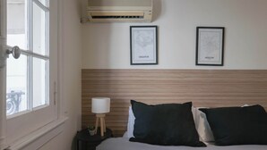 Een hotelkamer met een bed, een nachtkastje met een lamp, en twee inlijstingen met kaarten aan de muur.