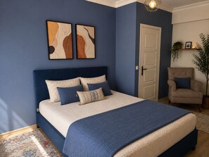 Een slaapkamer met een bed, een stoel, een deur en twee wanddecoraties.