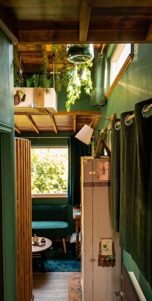 Ein gemütliches Interieur mit Holzbalkendecke, einer grünen Wand, einem Fenster mit Blick, einer Bank und einem Schrank mit einer Uhr.
