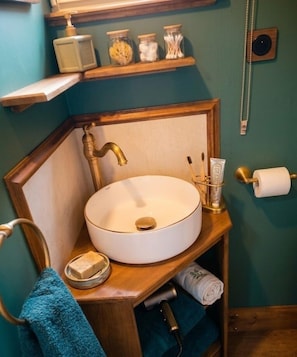 Et badeværelse med vask, træhylder, et håndklædetørrestativ og toiletpapirholder.