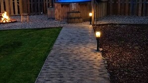 Un sendero de madera que lleva a un jacuzzi con cubierta azul, rodeado por una valla de madera y árboles.