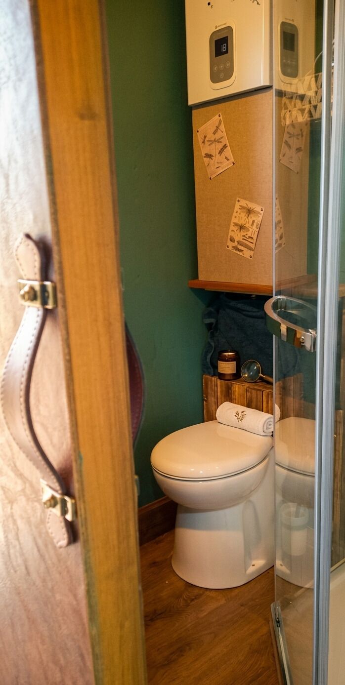 Une salle de bain comprenant des toilettes, un meuble en bois doté d’un thermostat numérique et une cabine de douche en verre.