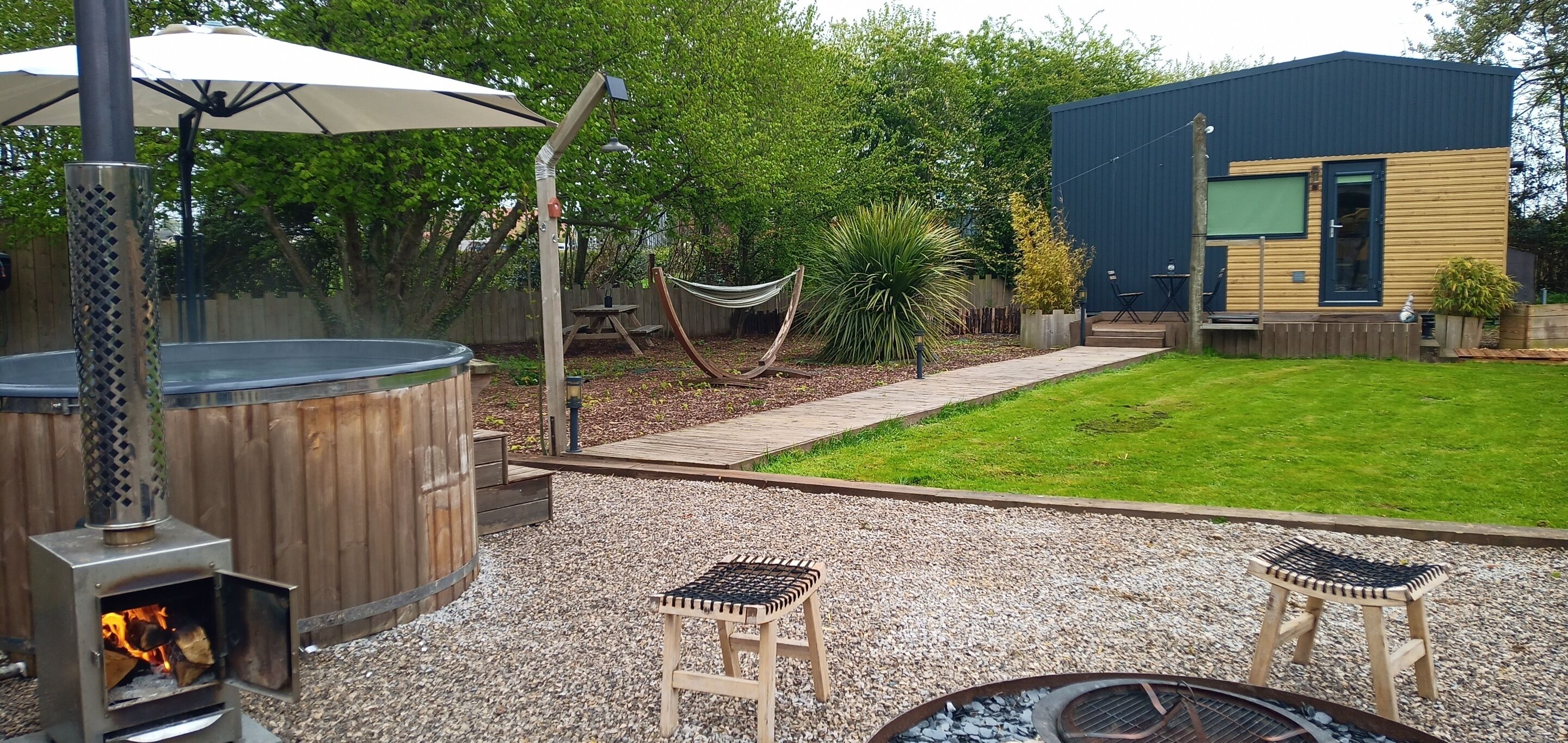 Un patio trasero con jacuzzi, terraza de madera, hamaca y una casa moderna.