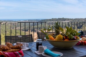 A table with croissants, a fruit bowl, and a view of a forested landscape.