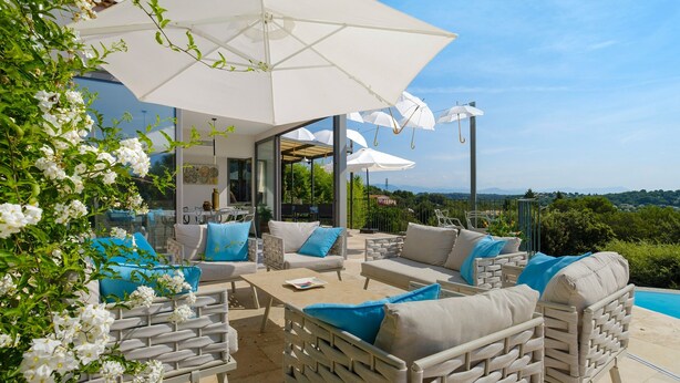 An outdoor seating area with white wicker furniture, blue cushions, and white umbrellas. - Villa "Le Panorama d’Azur – Pool" with Sea View, Wi-Fi, and Air Conditioning (Valbonne)