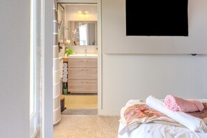 A bedroom with a bed, a bedside table, a wall-mounted TV, and a bathroom visible through an open door.