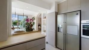 A modern kitchen with a stainless steel refrigerator, a countertop with a vase of flowers, and a view of the outdoors. - Villa "Le Panorama d’Azur – Pool" with Sea View, Wi-Fi, and Air Conditioning (Valbonne)
