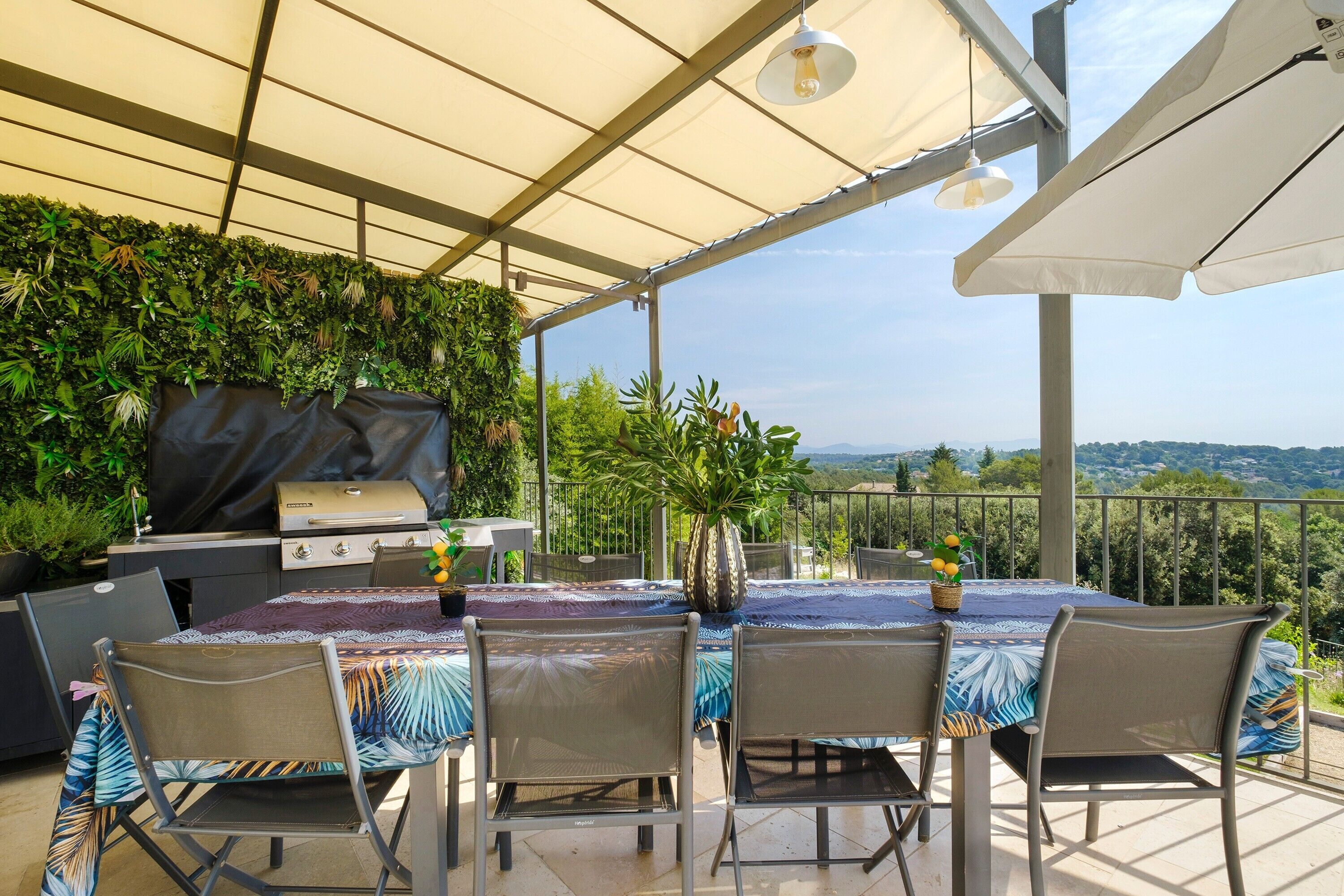 An outdoor patio with a grill, dining table, chairs, and a view of the landscape.
