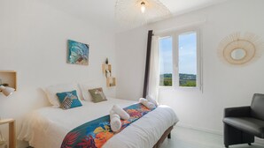 A bedroom with a bed, a chair, a window, and a painting on the wall. - Villa "Le Panorama d’Azur – Pool" with Sea View, Wi-Fi, and Air Conditioning (Valbonne)