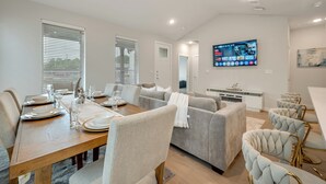A modern dining area with a wooden table set for four, a grey sofa, and a television mounted on the wall.