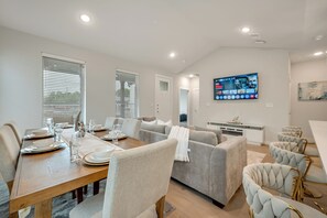 A modern dining area with a wooden table set for four, a grey sofa, and a television mounted on the wall.