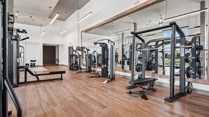 A gym with various exercise machines, wooden flooring, and large mirrors.