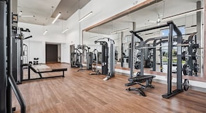 A gym with various exercise machines, wooden flooring, and large mirrors.