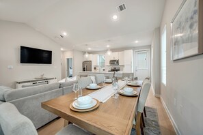 A modern kitchen with white cabinets, a flat-screen TV, and a dining area with a wooden table set for four.