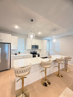 A modern kitchen with white cabinetry, stainless steel appliances, and a central island with bar stools.