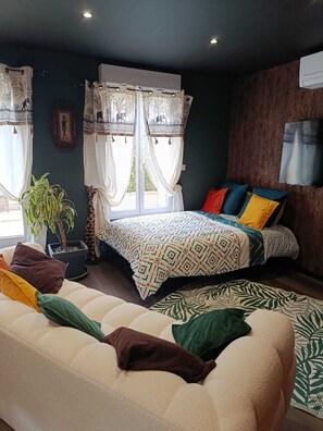 A bedroom with a bed, a sofa, a potted plant, and a window with curtains.