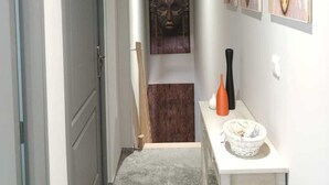 Käytävä, jossa on ovi, pieni pöytä maljakkoineen ja taideteoksia seinällä.