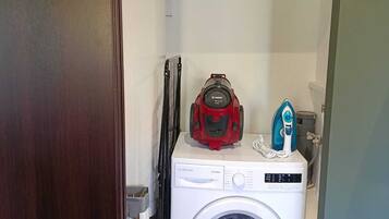 A laundry area with a washing machine, a red Bosch vacuum cleaner, and a blue iron on top.