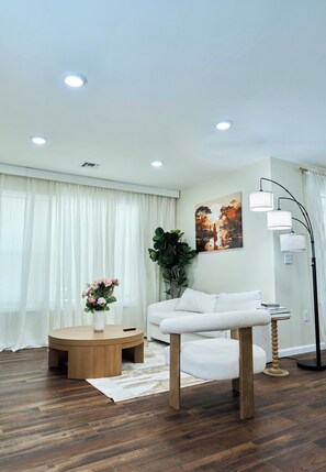 A modern living room with a white sofa, a round coffee table, a floor lamp, and a painting on the wall.