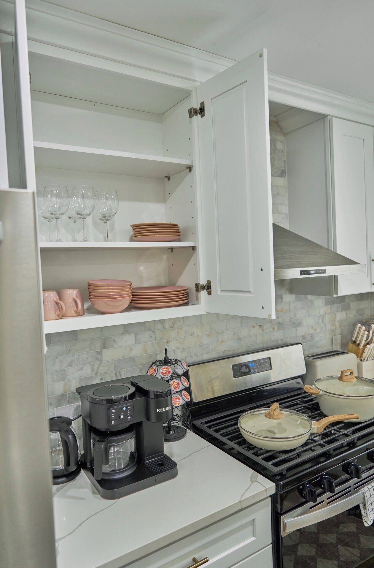 Una cocina con armarios blancos, una cafetera, una estufa y un salpicadero de azulejos.