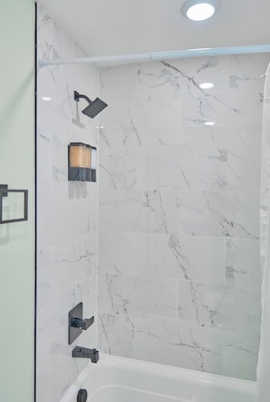 A modern bathroom with a shower, a bathtub, and a wall-mounted light fixture.