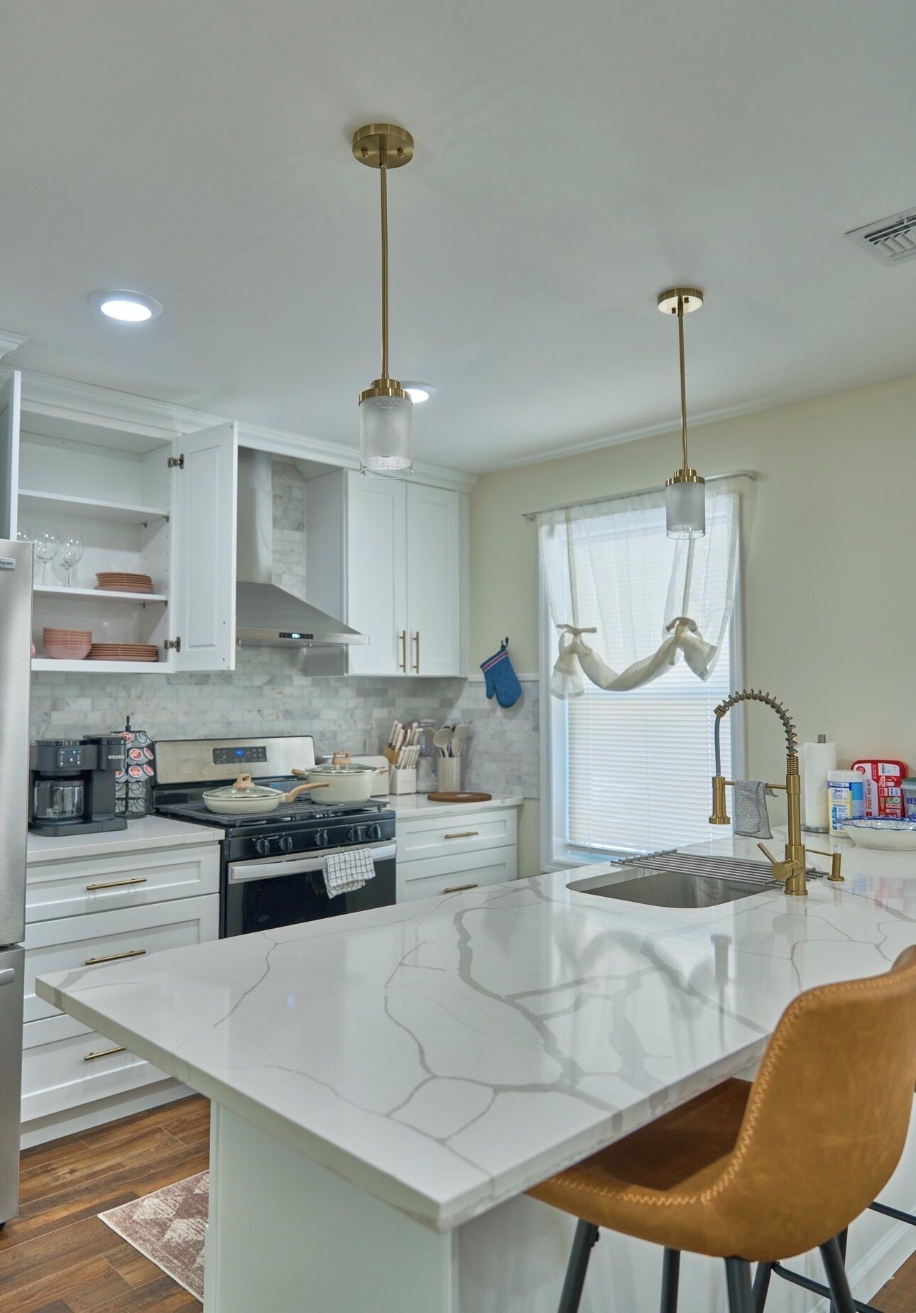 A modern kitchen with white cabinetry, a central island, a stove, and a sink with a gold faucet.