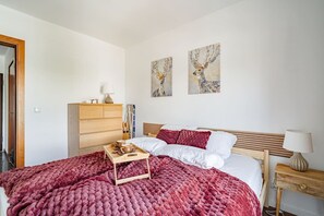 Une chambre à coucher comprenant un lit, une commode en bois, une table de chevet et deux tableaux accrochés au mur.